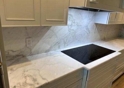 White kitchen countertop with marble-pattern backsplash and a black glass-ceramic cooktop; white upper and lower cabinets surrounding the space.